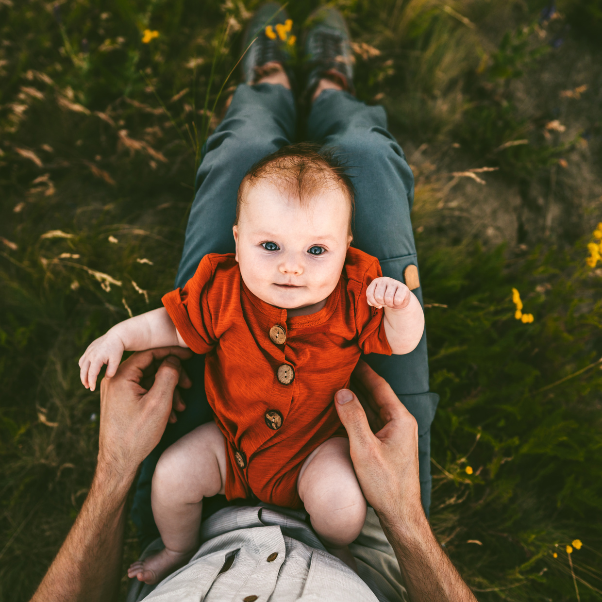 Une image d'un bébé en costume rouge, allongé sur les genoux de son père et levant les yeux